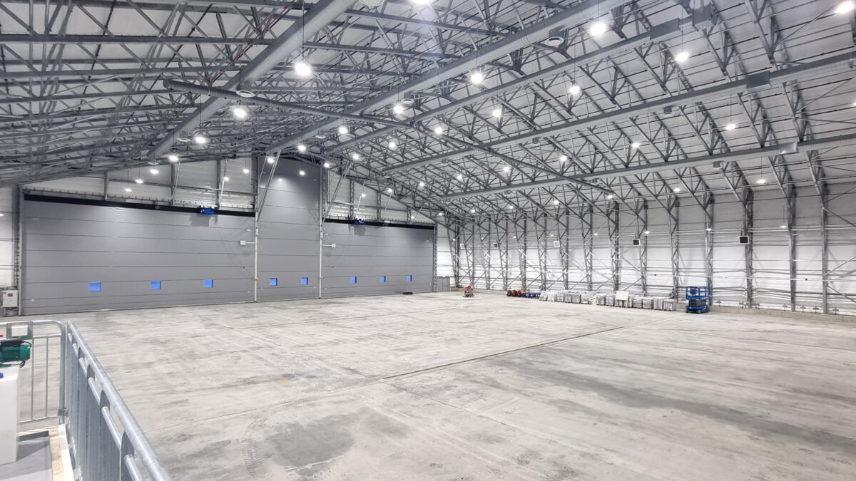 A spacious hangar, illuminated with bright white lights, offers ample space for various uses. Hallgruppen has designed this structure to meet specific needs.