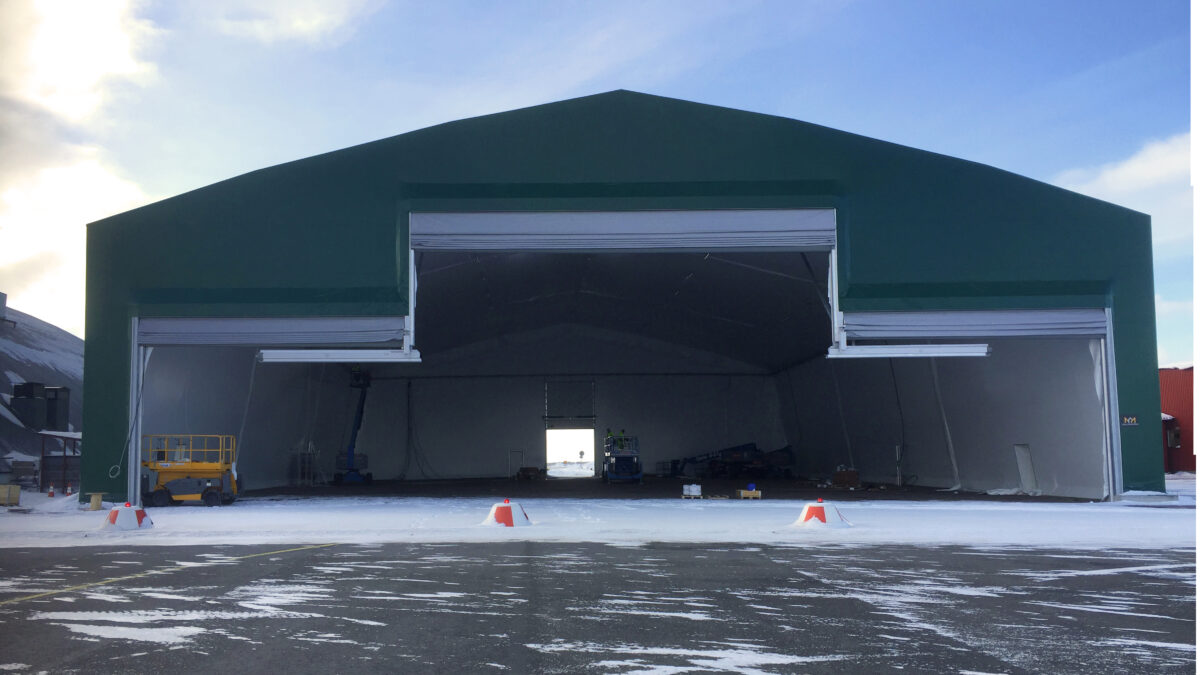 A large green hangar with open doors, demonstrating its use for larger vehicles or equipment. Hallgruppen is behind this robust construction.